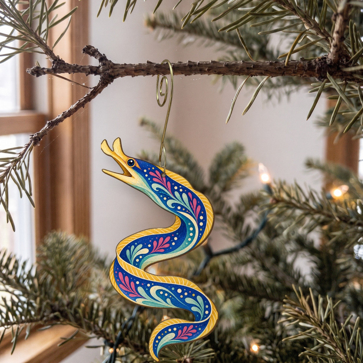Laser-cut maple wood Ribbon Eel folk art ornament O149 hanging on a fir branch, made in USA