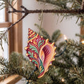 Laser-cut maple wood Conch folk art ornament O174 hanging on a fir branch, made in USA