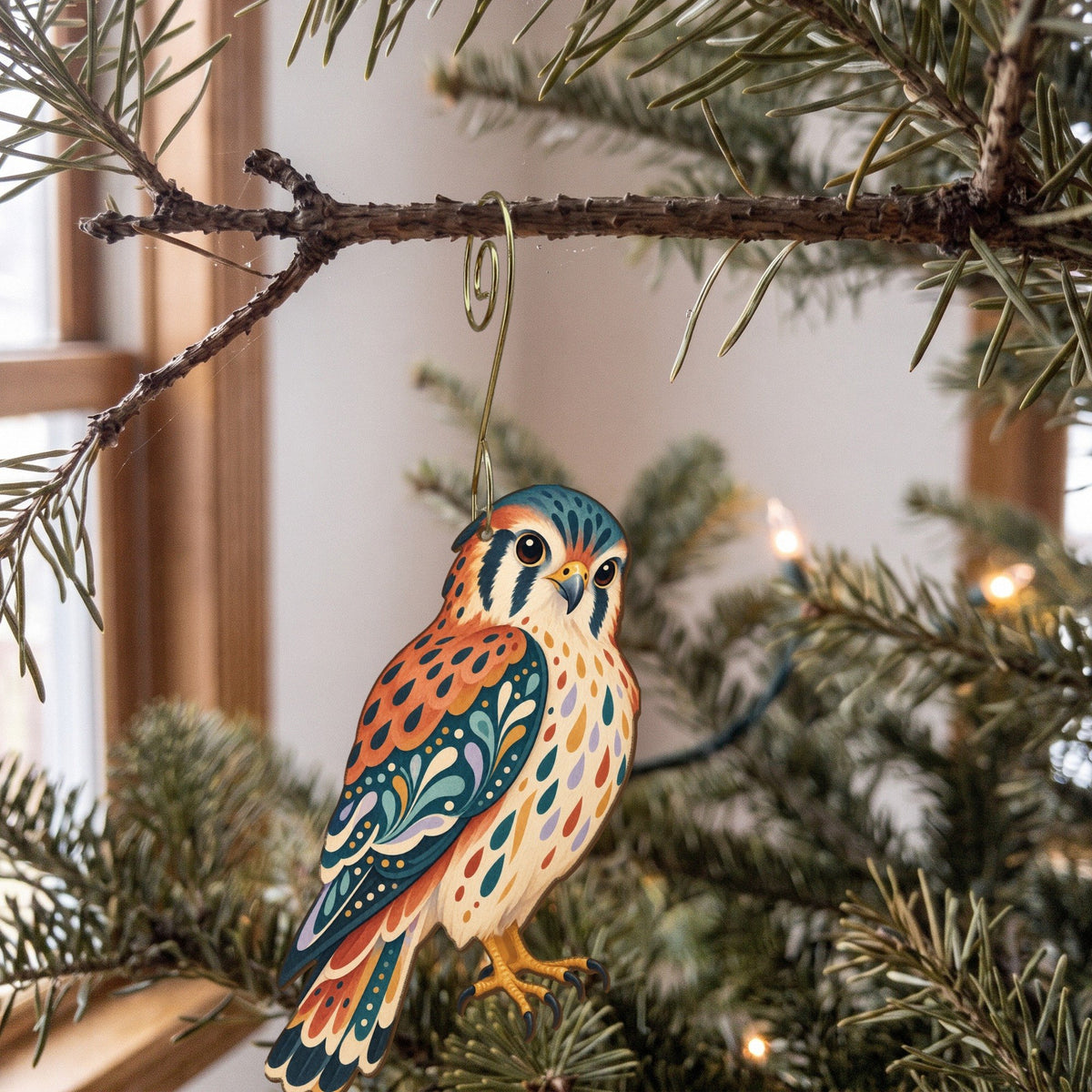 Laser-cut maple wood American Kestrel folk art ornament O295 hanging on a fir branch, made in USA