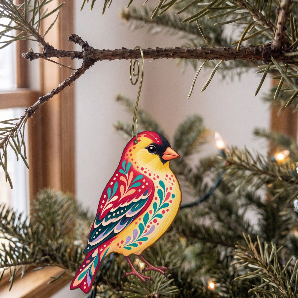 Laser-cut maple wood American Goldfinch folk art ornament O312 hanging on a fir branch, made in USA