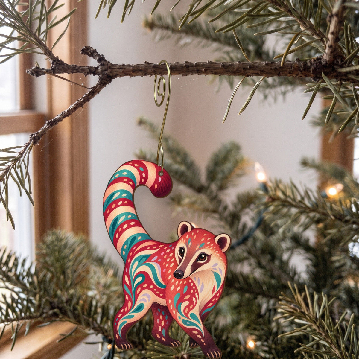 Laser-cut maple wood Coati folk art ornament O408 hanging on a fir branch, made in USA
