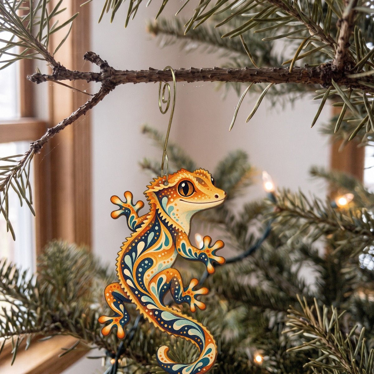 Laser-cut maple wood Crested Gecko folk art ornament O530 hanging on a fir branch, made in USA